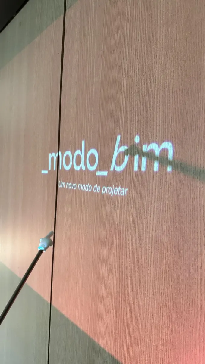 Slide da _modo_bim projetado em uma parede de madeira, com o wordmark e a assinatura “Um novo modo de projetar”