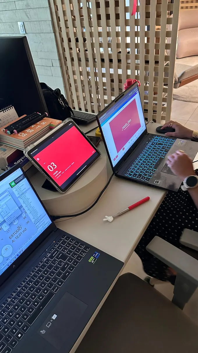 Mesa de trabalho com notebooks e um tablet, telas mostrando o material da _modo_bim