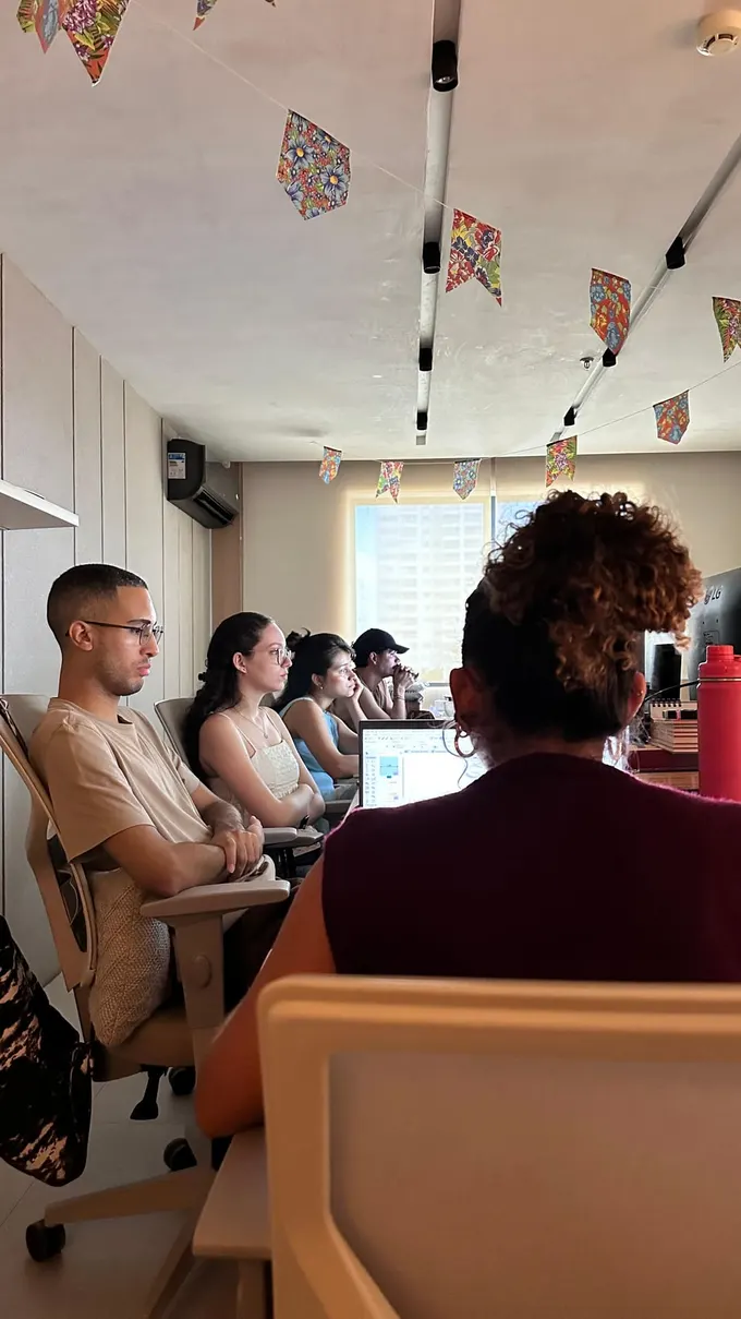 Turma acompanhando uma apresentação em uma sala clara, com bandeirinhas de festa junina no teto